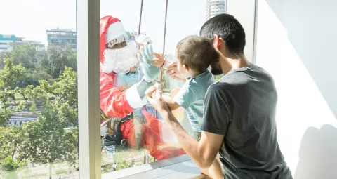 Viejito pascuero saludando a niño por la ventana en Clínica Santa María.