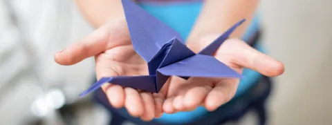 Manos sosteniendo una grulla de papel. 