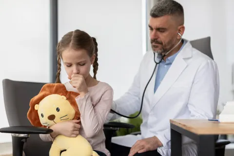 Médico auscultando a niña que tose