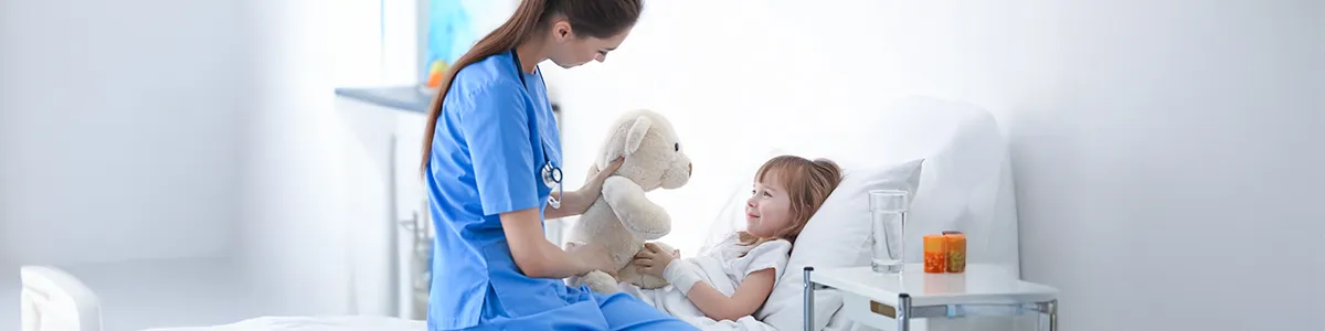 Doctora jugando con una niña con un oso de peluche. Especialidad Cirugía Pediátrica